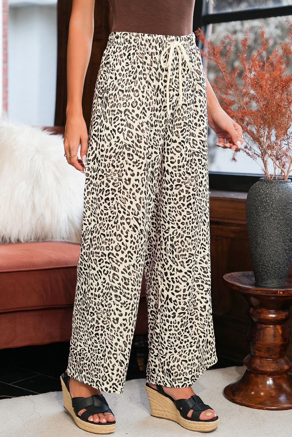 Woman wearing Brown Leopard Drawstring Loose Pants by a sofa and dried flowers, paired with black wedge sandals.